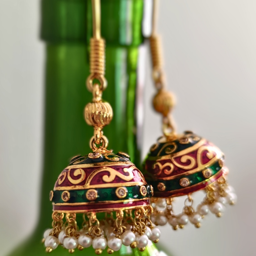 Gold and red earrings with pearl details on a green bottle background