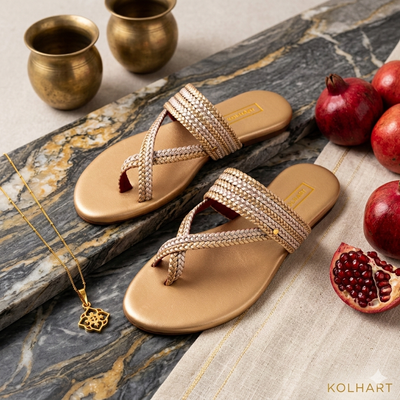 Beige sandals with decorative straps on a marble surface with pomegranates and brass cups along with silver pendant and chain 