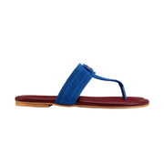 A single thong sandal shown in profile against a solid white background. The sandal features a vibrant blue suede strap with a small gold-tone circular logo detail, resting on a deep burgundy-red footbed with a light tan outsole.