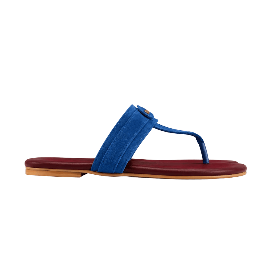 A single thong sandal shown in profile against a solid white background. The sandal features a vibrant blue suede strap with a small gold-tone circular logo detail, resting on a deep burgundy-red footbed with a light tan outsole.