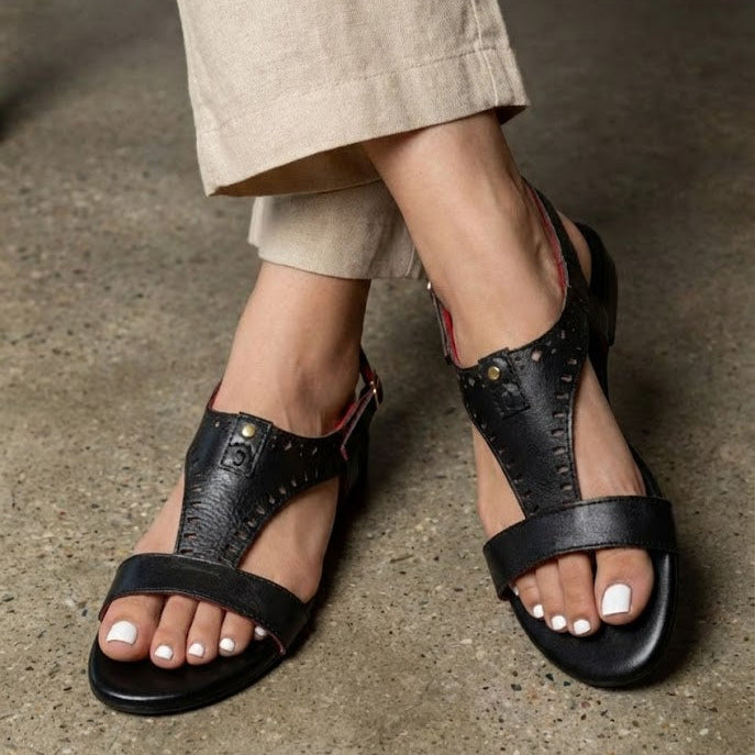 Black sandals worn with beige pants on a concrete floor