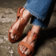 Brown sandals worn with blue jeans on a textured floor.