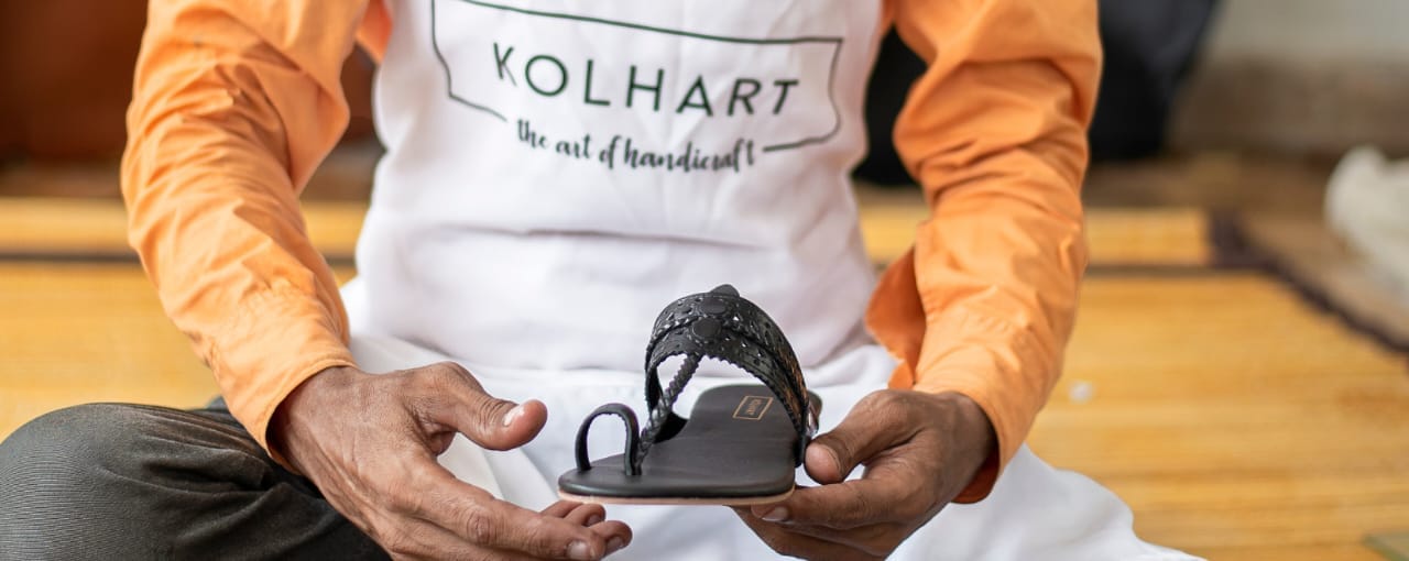 Person holding a sandal with 'Kolhart' branding, wearing an apron.