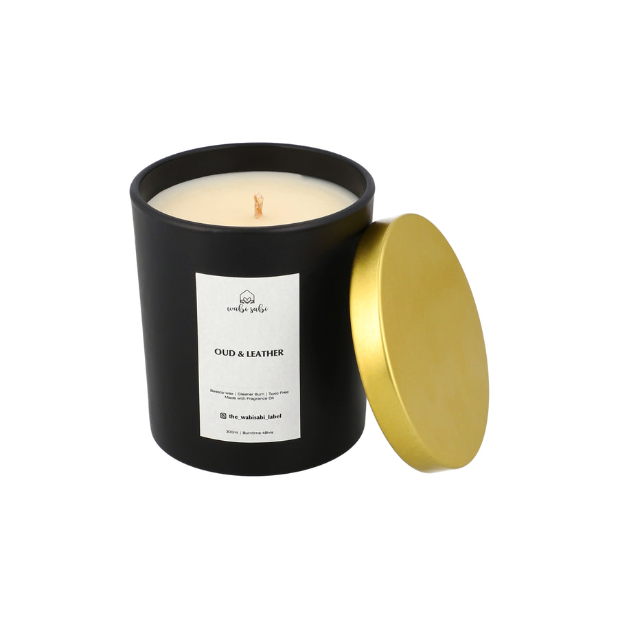 Black candle jar with a lit candle inside, gold lid, and 'Oud & Leather' label on a white background.