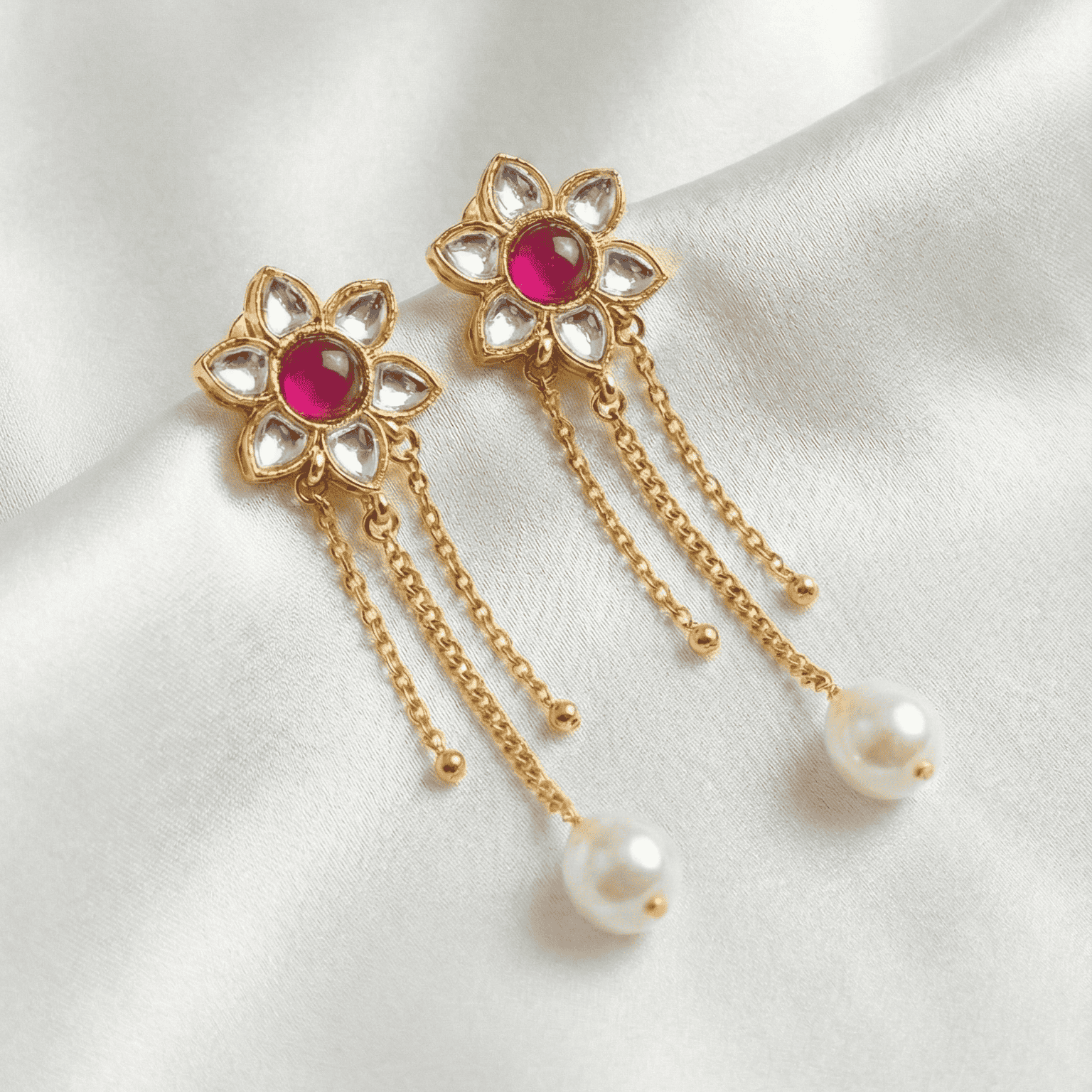 Gold earrings with red gemstones and pearl drops on a white satin background